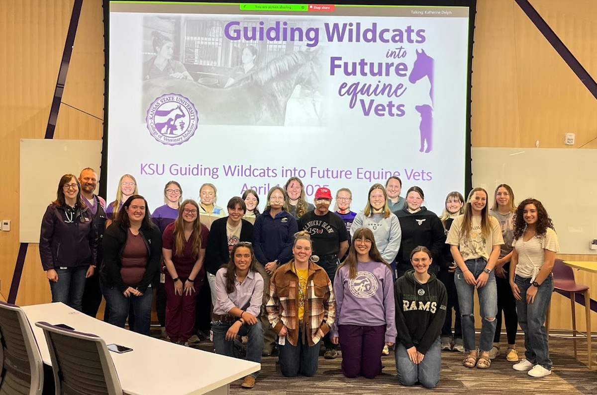 A group of students and faculty pose together in a classroom in front of a presentation screen reading “Guiding Wildcats into Future Equine Vets.” Everyone is smiling and some are wearing purple or animal-themed clothing.